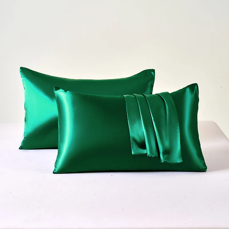 A set of two emerald green satin pillowcases lying on a white surface.