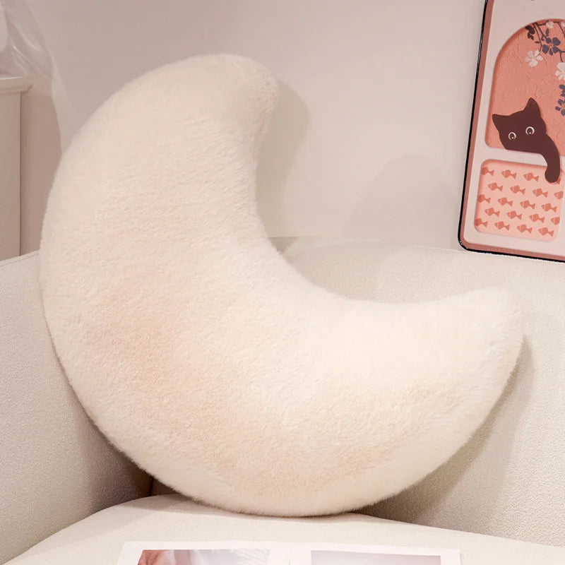 A fluffy white moon-shaped throw pillow resting on a light-colored surface.