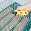 A hand holds a yellow precision acrylic quilting ruler with a dual scale and seam rail placed on a green cutting mat.