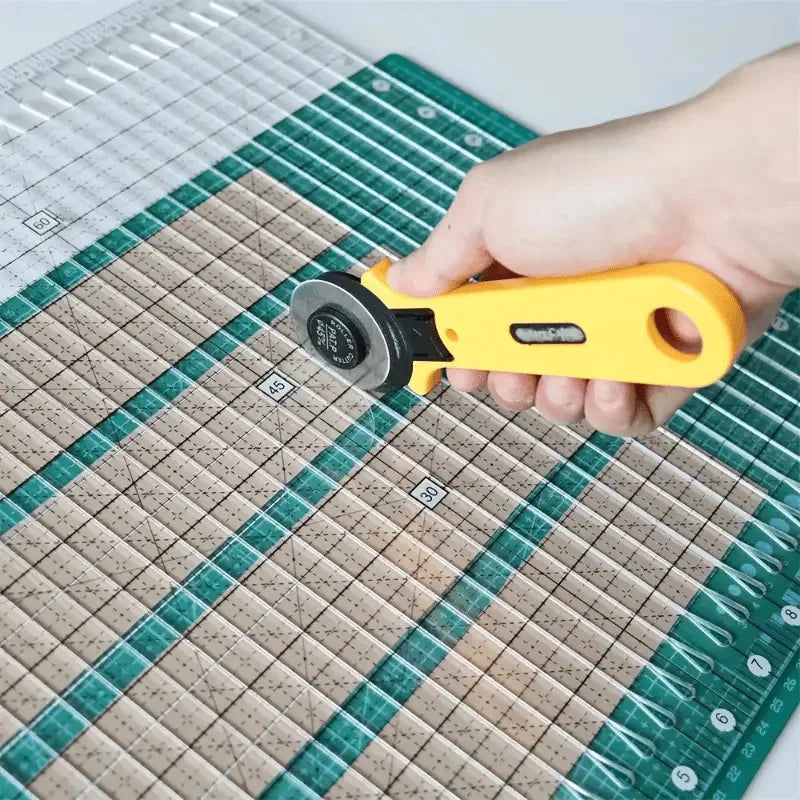 A hand holds a yellow precision acrylic quilting ruler with a dual scale and seam rail placed on a green cutting mat.