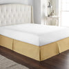 A modern bed featuring a thick, cream-colored upholstered headboard and a beige mattress with a gold-toned skirt.
