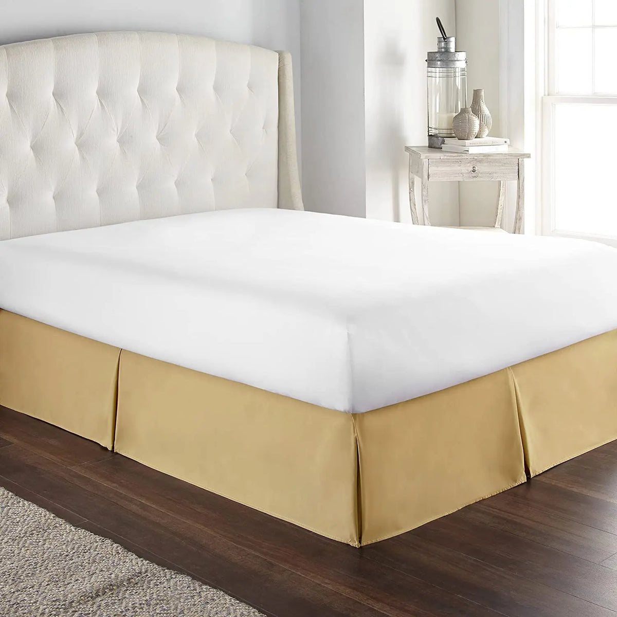 A modern bed featuring a thick, cream-colored upholstered headboard and a beige mattress with a gold-toned skirt.