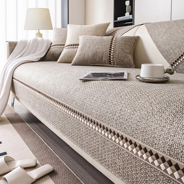 A beige linen sofa cover with neutral pillows and a white throw blanket on a modern sofa.