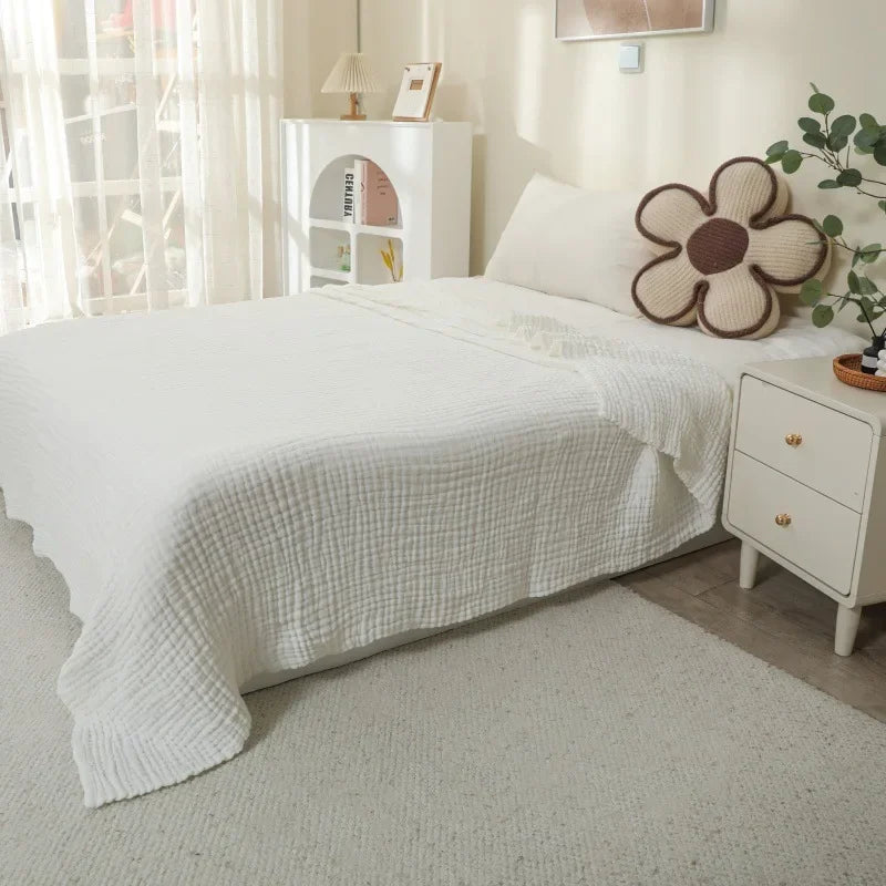 A white bed with a white quilted blanket and a large, round, brown floral cushion on the bed.