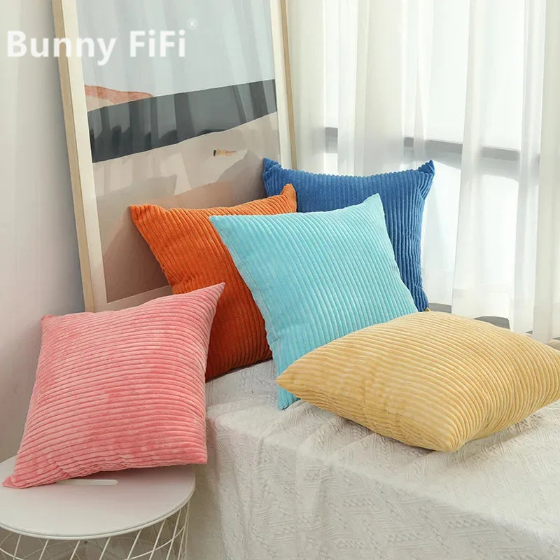 A collection of colorful corduroy striped throw pillows in shades of orange, teal, and blue displayed on a white surface.