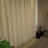 Light beige sheer curtains with a star pattern overlay hanging in a room.