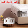 A white bed sheet holder device is shown next to a bed, used for securing sheets.