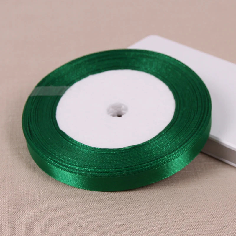 A roll of green satin ribbon for crafting and decoration is shown on a light background.