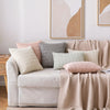 A collection of cream, beige, and dusty rose decorative throw pillows arranged on a light-colored sofa.