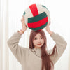 A woman holds a plush volleyball ball cushion with red and green stripes above her head.