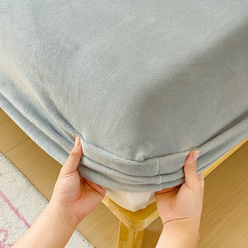 Hands are folding a light gray flannel fitted sheet with deep pockets on a wooden surface.