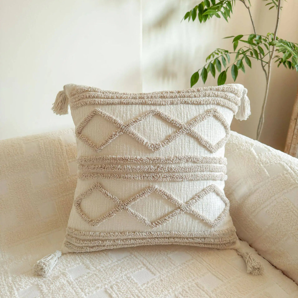 A cream knit pillow cover with diamond stitching rests on a light-colored sofa.