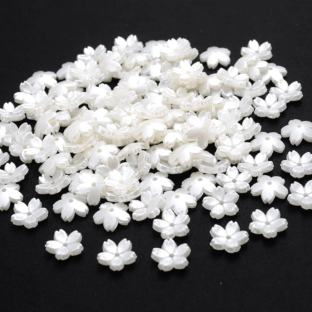 A pile of small, white imitation pearl flower spacer beads for DIY jewelry.