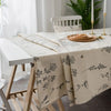 A beige botanical print linen tablecloth is draped over a white wooden table.