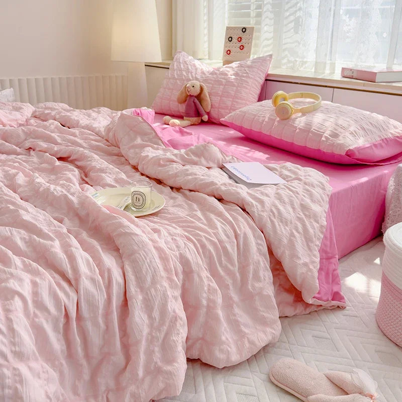 A pink summer seersucker quilt comforter spread out on a bed with a stuffed animal pillow and yellow headband.