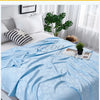 Light blue bamboo fiber blanket draped over a white bed with green plants and sheer curtains.