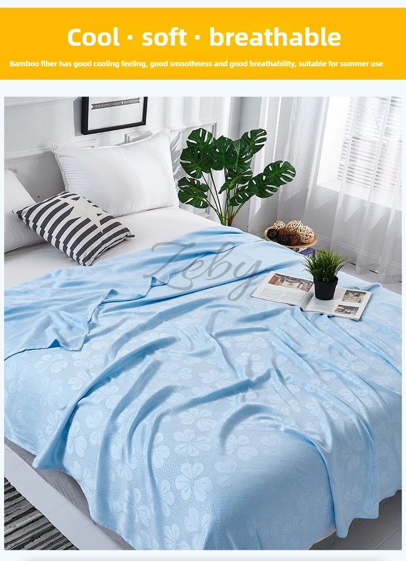 Light blue bamboo fiber blanket draped over a white bed with green plants and sheer curtains.