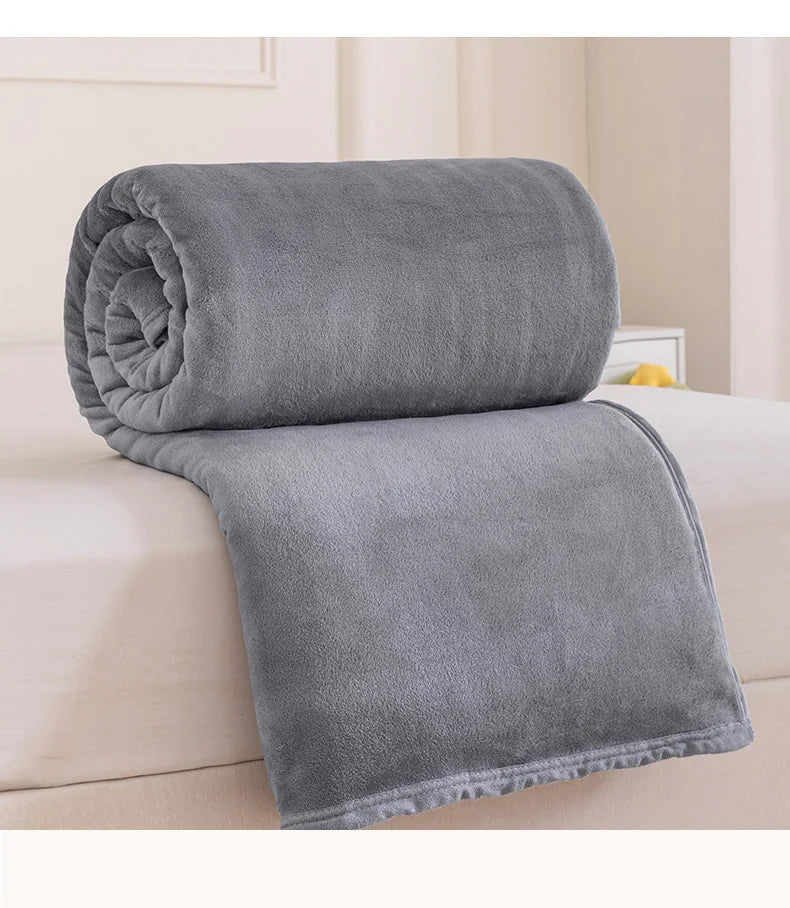 A rolled and unfolded gray flannel throw blanket resting on a white bed.