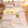 A light-colored striped quilt set featuring pink, green, and beige stripes with a yellow blanket on a bed.