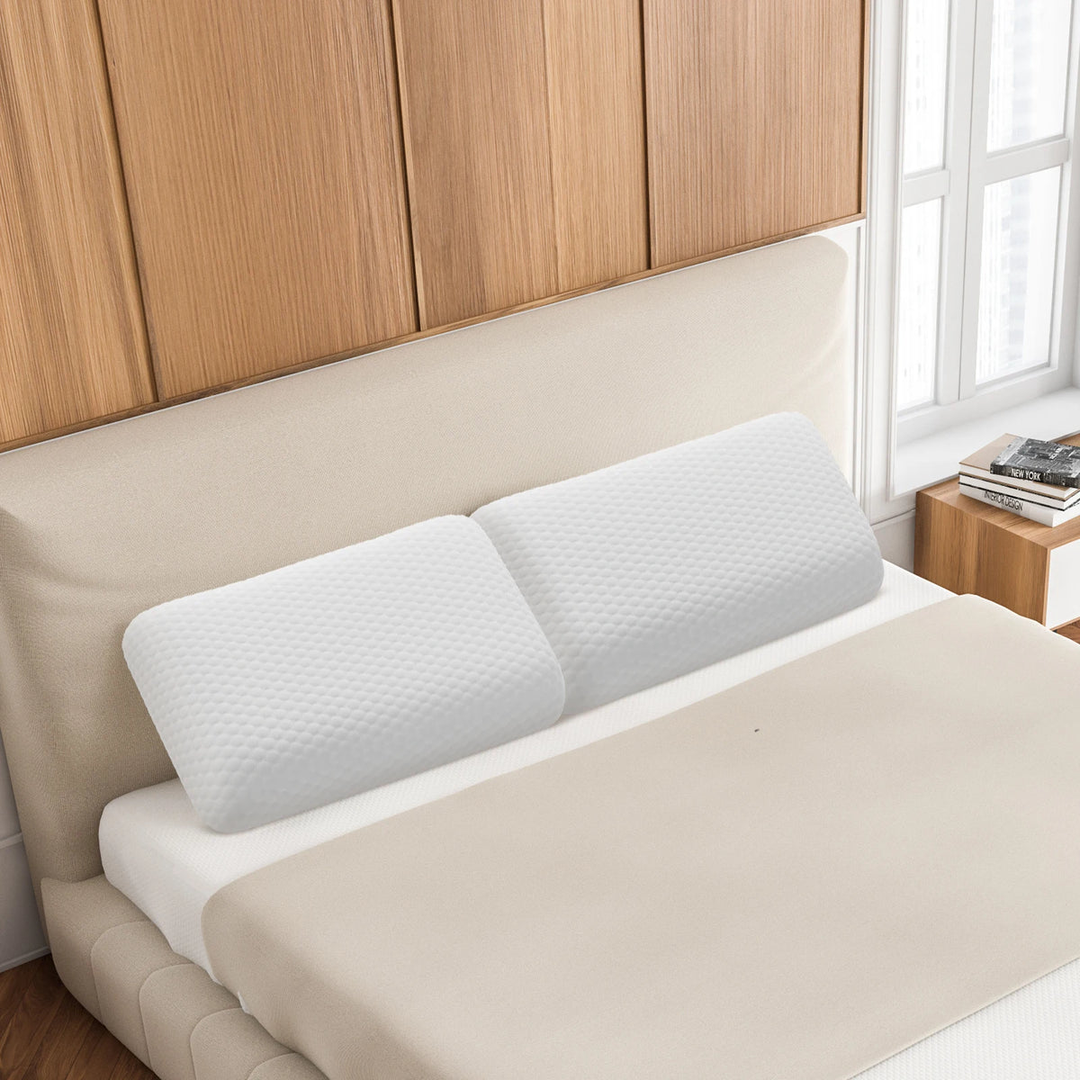 A beige memory foam neck pillow with a white textured cover is displayed on a bed.