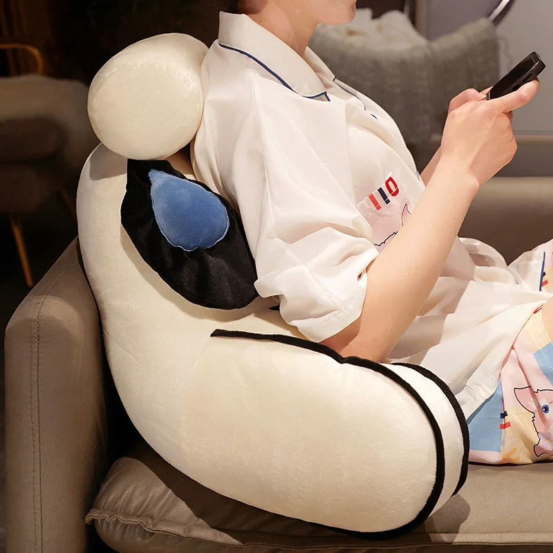 A person is relaxing on a light-colored sofa, leaning against a large, round plush cushion with black and blue accents.
