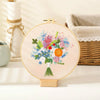 A circular embroidery hoop displaying a colorful floral bouquet of blue, pink, and orange flowers on a light beige fabric.