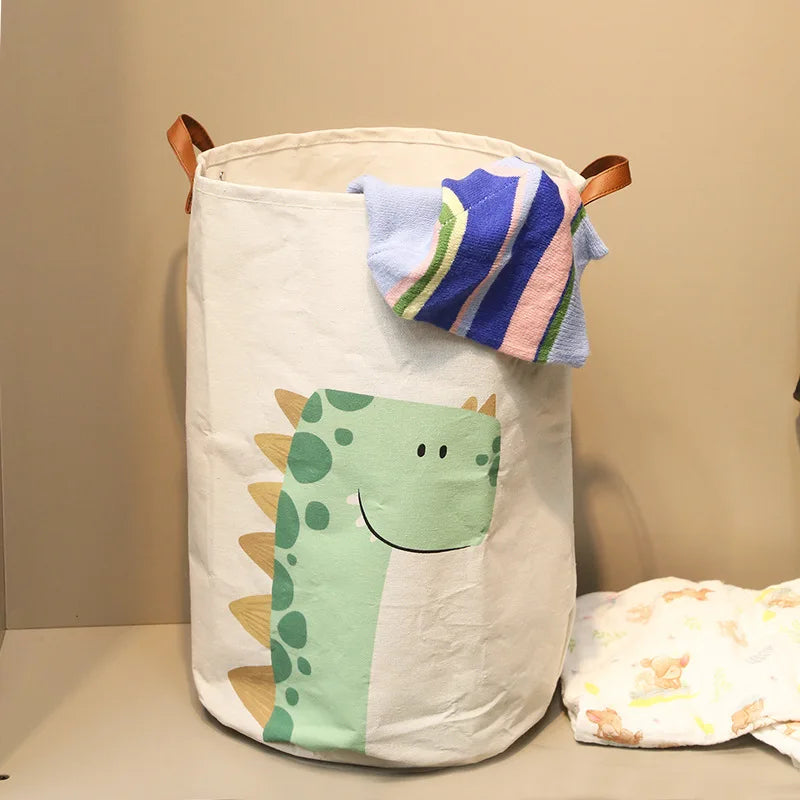 A white storage basket with a dinosaur face design and colorful fabric attached, used for baby or dirty clothes.