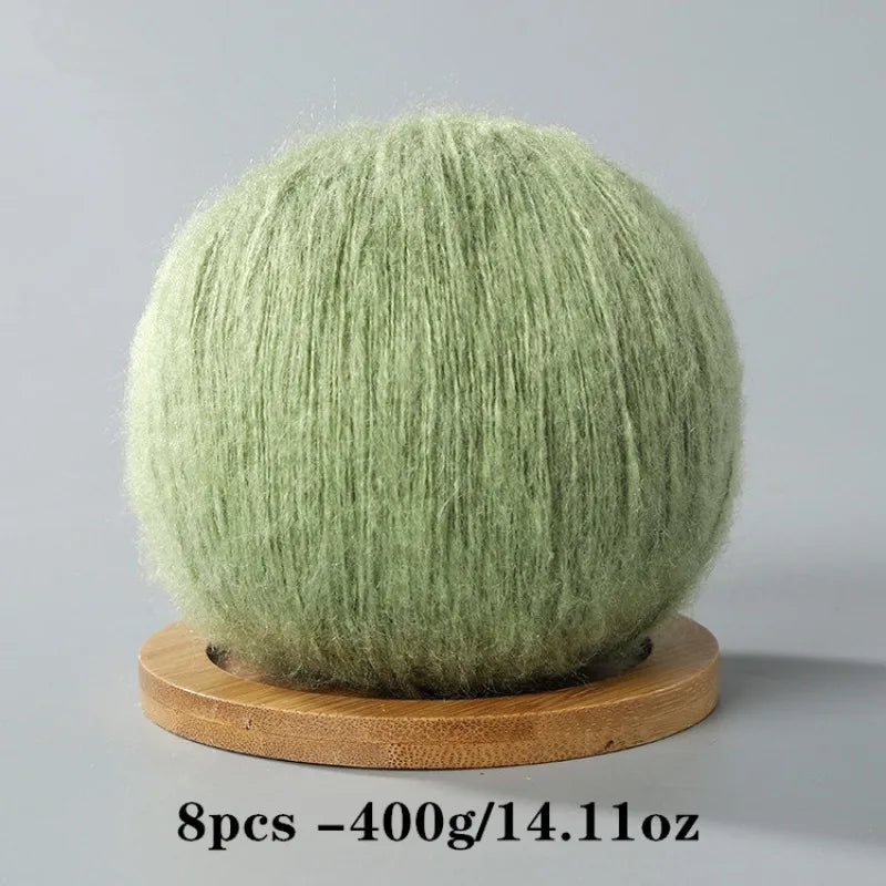 A ball of light green mohair yarn used for crafting, displayed on a wooden base.