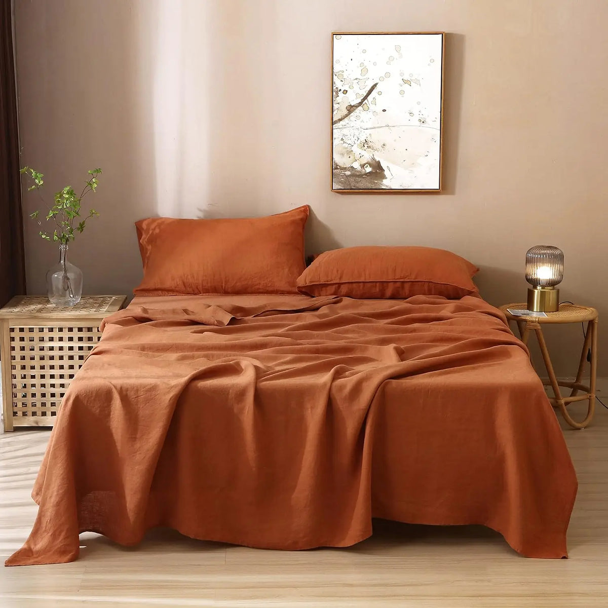 A bed dressed with an orange linen bedding set featuring a neutral abstract artwork above the headboard.