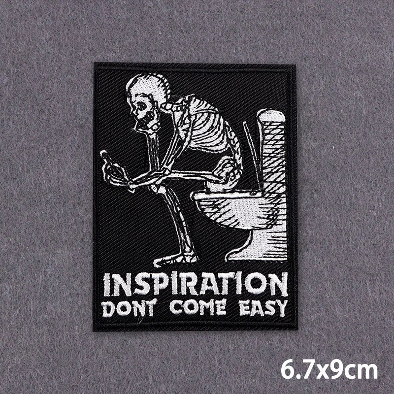 Black embroidered patch featuring a skeletal hand holding a toilet, with the text INSPIRATION DON'T COME EASY.