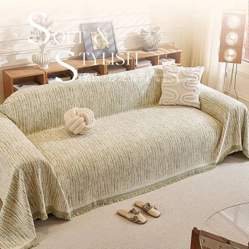 A light beige jacquard sofa cover blanket draped over a sofa in a bright living room setting.