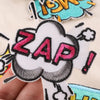 A close-up of a black and white embroidery patch featuring the word ZAP on a cloud design.
