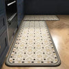 A rectangular beige and gray anti-slip floor mat placed on a light wood floor next to dark cabinetry.