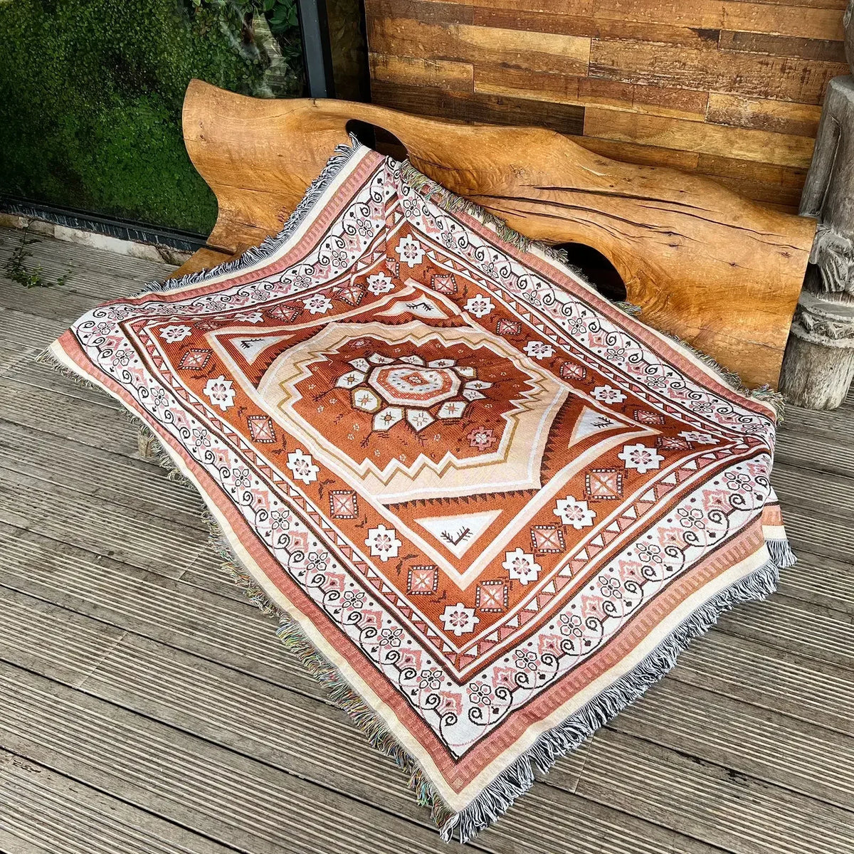 A geometric patterned throw blanket with earthy tones laid on a wooden deck next to a large wooden carving.