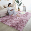 A pink faux fur rug is placed on a light wood floor in a living room setting with a woman reading.
