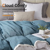 A soft blue throw blanket is draped over a bed, with several pillows and a white plant visible.