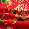 Close-up of red linen fabric with a floral print featuring orange and yellow roses.