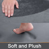 Close-up view of a gray memory foam bathroom mat showing a hand and a bare foot pressing into the soft surface.