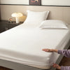 A white fitted sheet is laid on a bed, with hands adjusting the fabric near the edge.