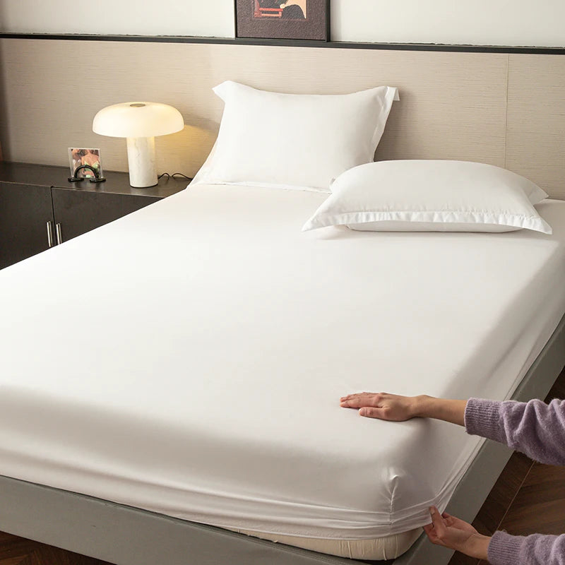 A white fitted sheet is laid on a bed, with hands adjusting the fabric near the edge.
