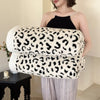 A woman models a thick leopard print jacquard knit throw blanket draped over her arm.