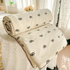 A cream-colored quilt blanket with a subtle black pastoral print is rolled and displayed on a white draped surface.