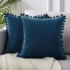 A dark teal velvet decorative cushion cover with tasseled trim resting on a light fabric.