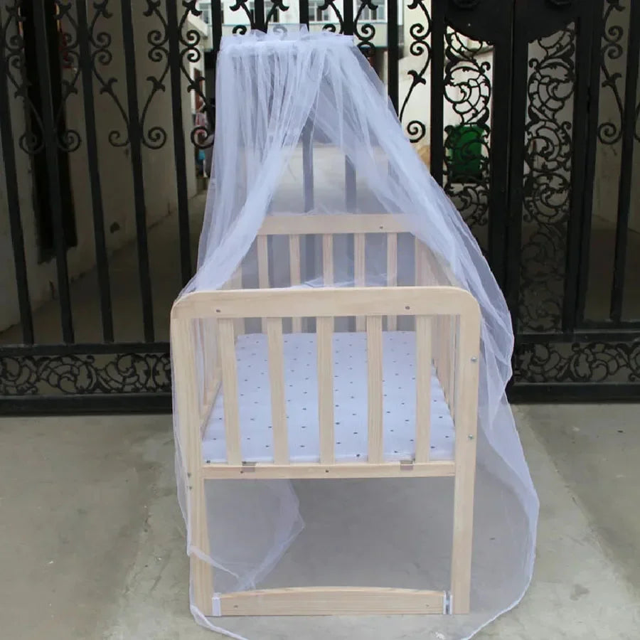 A wooden crib covered with a sheer white mosquito net, displayed in a doorway.