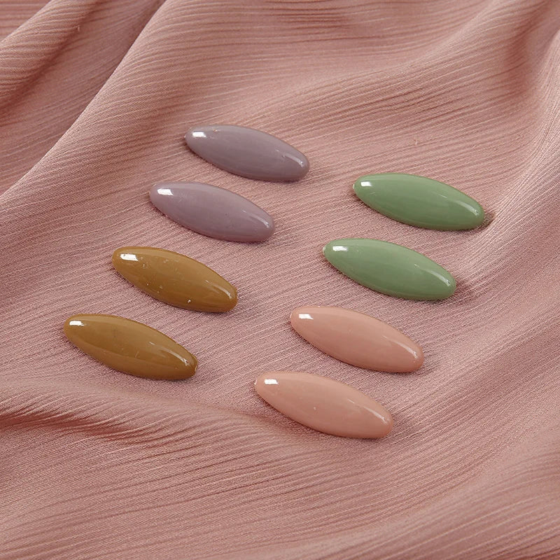 Eight plastic safety pins in various pastel shades of pink, green, and yellow arranged on a pink fabric.