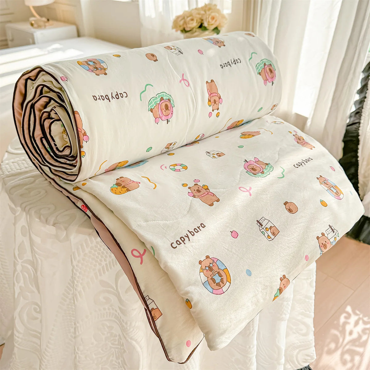 A rolled and unfolded cream-colored quilt blanket featuring a pastoral print design with cute animal illustrations.