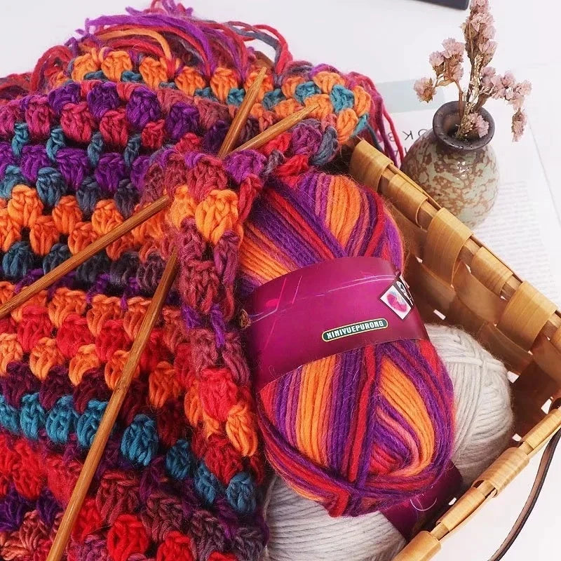 A ball of gradient dyed wool yarn in vibrant colors is shown next to bamboo knitting needles and a woven basket.
