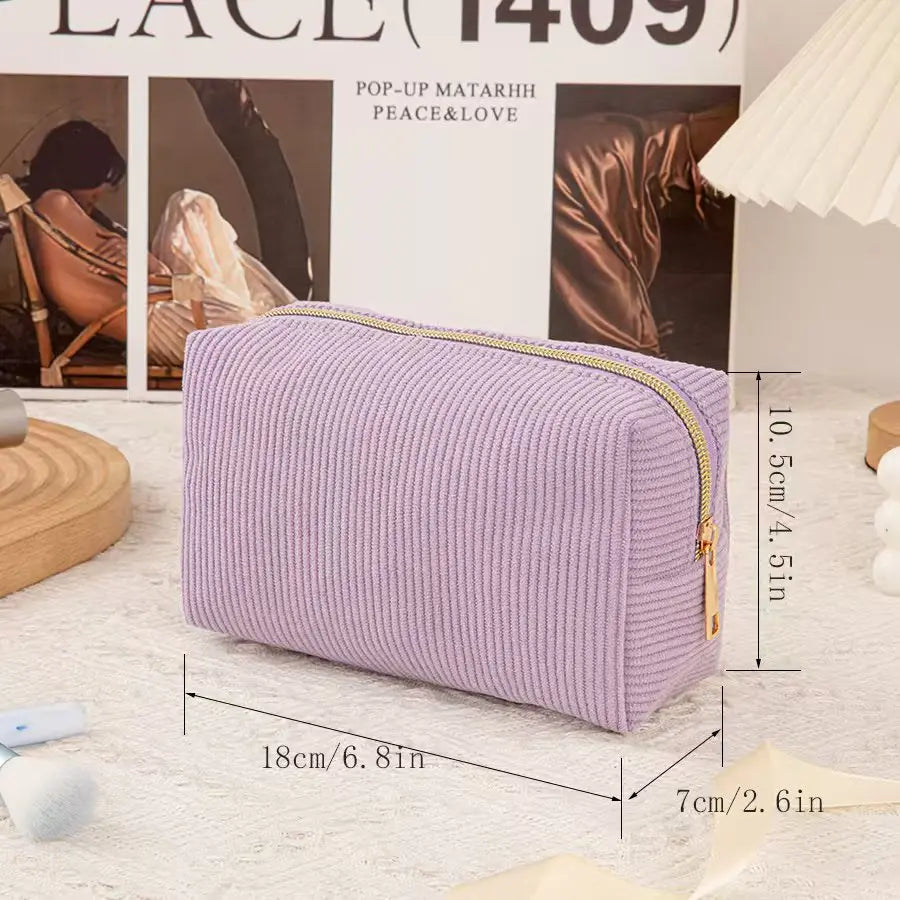 A lavender textured cosmetic storage pouch with a gold zipper is displayed on a white surface.