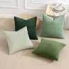 A set of four textured throw pillows in shades of olive green and sage green on a light beige sofa.