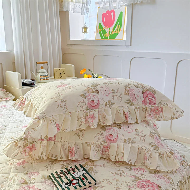 Two floral cotton pillow covers in pale pink and green patterns displayed on a bed.